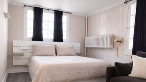 A bedroom with a bed, bedside tables, a radiator, and a window with curtains. - Hidden Gem in the Heart of Capitol Hill (Denver)