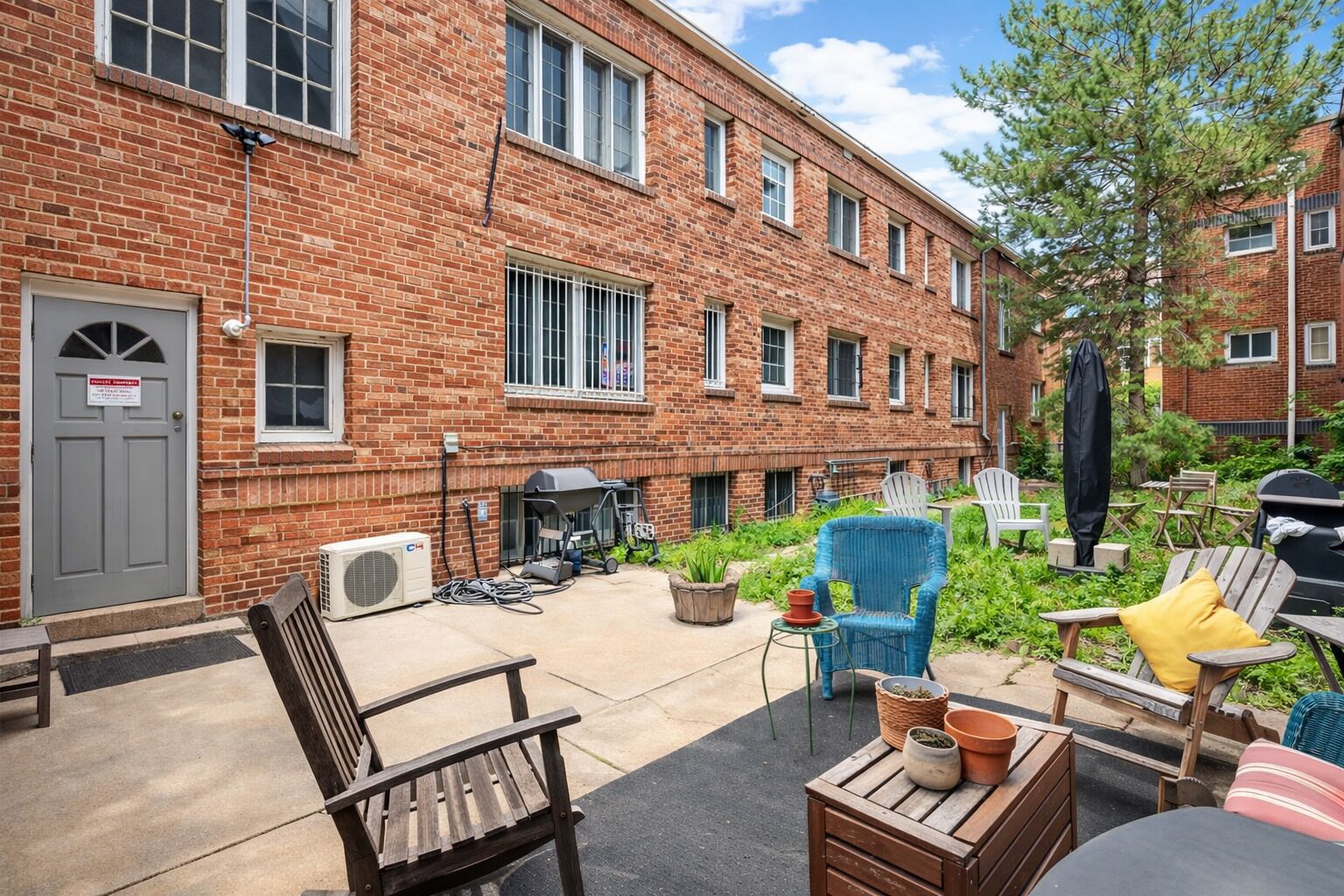 A brick building with multiple windows, outdoor seating with chairs and tables, and a grill area.
