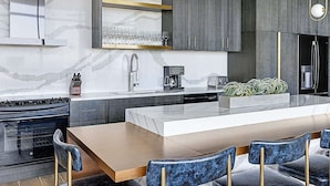Una cocina moderna con una isla central, electrodomésticos de acero inoxidable y un comedor con sillas azules.