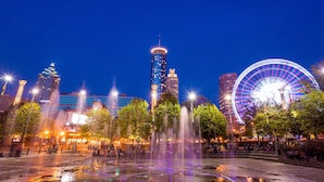 Un paisaje urbano con una fuente destacada, edificios iluminados y una noria grande.