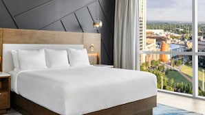 Una habitación de hotel moderna con una cama grande, una mesita de noche de madera y vistas a la ciudad.