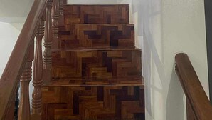 Eine hölzerne Treppe mit einem geometrischen Muster, ein Fenster mit einem Kreuz und ein an der Wand befestigtes Kreuz.