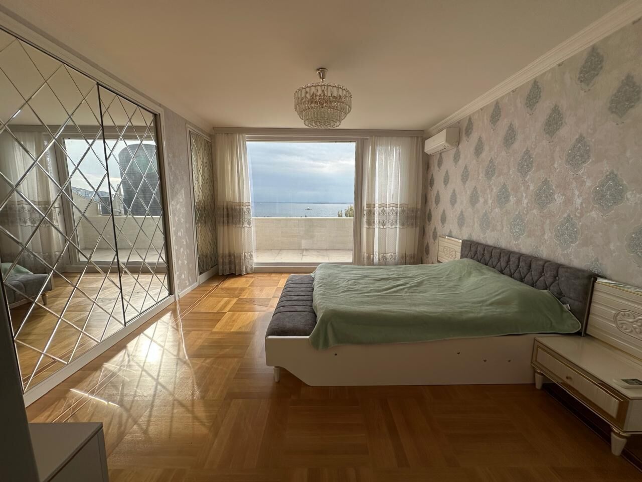 Un dormitorio con cama, mesita de noche, cómoda, balcón con vistas y candelabro.