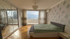 Ein Schlafzimmer mit Bett, Nachttisch, Schminktisch, einem Balkon mit Blick und einer Chandelier.