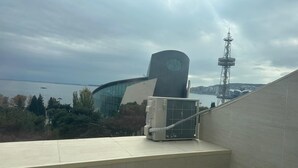 Ein modernes Gebäude mit einer gewölbten Fassade und einem Uhrturm, das auf ein Gewässer blickt.