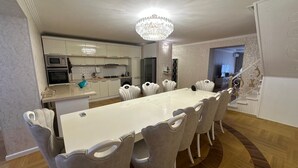 Ein Essbereich mit einem langen Tisch und Stühlen, einer Chandelierleuchtre und einer Küche im Hintergrund.