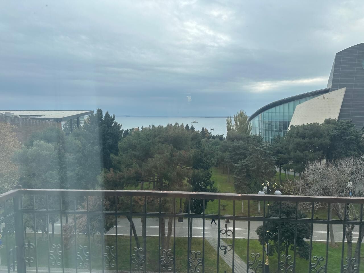A view from a balcony overlooking a road with trees and modern buildings in the background.
