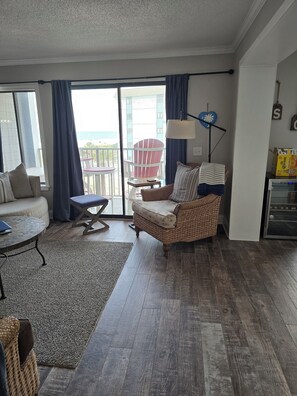 A living room with a wicker sofa, a small round table, a blue chair, a glass door leading to a balcony, and a lamp. - A308 at the Myrtle Beach Resort
Beautiful Oceanfront 2 bdrm condo. (Myrtle Beach)