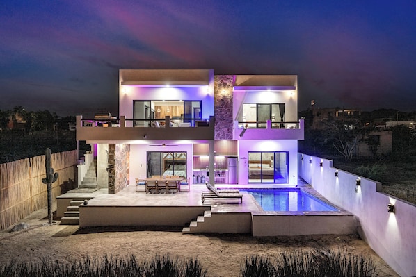 A modern two-story house with a swimming pool, outdoor seating, and a staircase leading to the upper level.