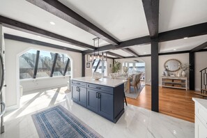 A spacious kitchen with a large island, dark cabinetry, and a view through a large window. - Luxury Waterfront - Hot Tub, Deck, Workspace, Waterview. Beautiful Sunsets! (Dennis)
