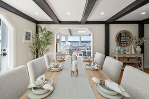 Ein Essbereich mit einem langen Tisch, gedeckt für sechs Personen, mit Blick auf das Meer und einem modernen Interieur.