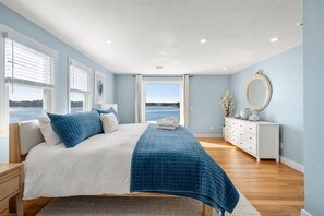Ein Schlafzimmer mit Bett, Kommode, Spiegel und Fenster mit Blick aufs Wasser.