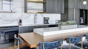 Una cocina moderna con una isla central, electrodomésticos de acero inoxidable y un comedor con sillas azules.