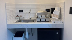 A compact kitchen with a sink, coffee maker, sugar container, and a trash bin. - Walk Everywhere , Budget Stay w/ AC + WiFi #1 (La Fortuna)