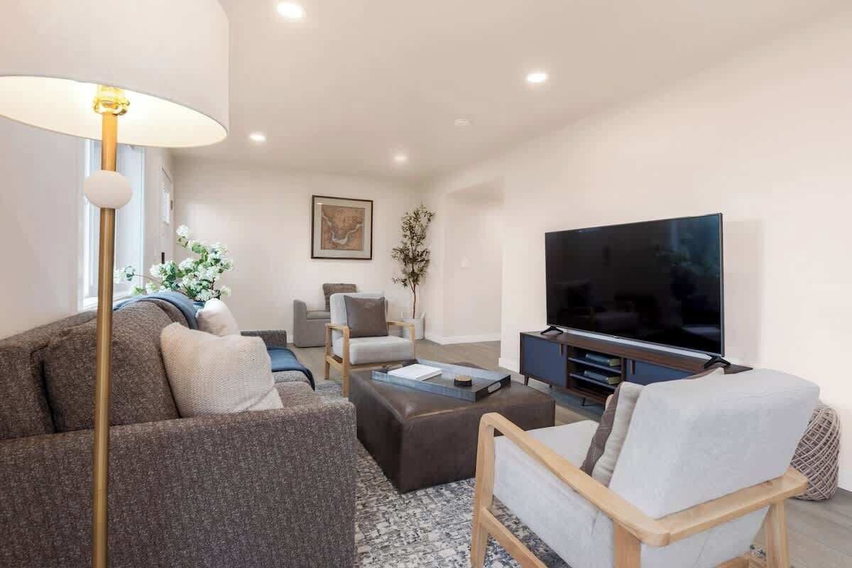 Una sala moderna con sofá, sillón, reposapiés, televisor y lámpara de pie.