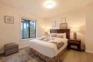Ein Schlafzimmer mit einem großen Bett, zwei Nachttischlampen, einem Fenster mit Ausblick und einem kleinen Hocker.