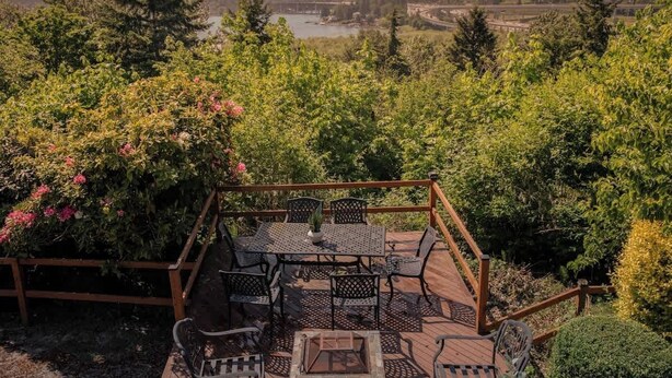 A deck with outdoor furniture, surrounded by lush greenery and a scenic view of a lake and hills. - Bright 2BR Lower Unit | Relaxing Yard & Great Spot (Bellevue)
