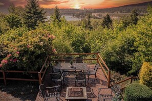 A deck with outdoor furniture, surrounded by lush greenery and a scenic view of a lake and hills. - Bright 2BR Lower Unit | Relaxing Yard & Great Spot (Bellevue)