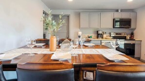 A dining area with a wooden table set for four, a vase with greenery, and a kitchen in the background. - Bright 2BR Lower Unit | Relaxing Yard & Great Spot (Bellevue)