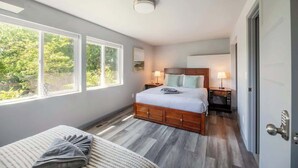 A bedroom with a large window, a bed, a bedside table, and a door. - Bright 2BR Lower Unit | Relaxing Yard & Great Spot (Bellevue)