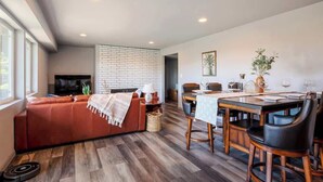 A modern living room with a sofa, dining table, chairs, and a TV. - Bright 2BR Lower Unit | Relaxing Yard & Great Spot (Bellevue)