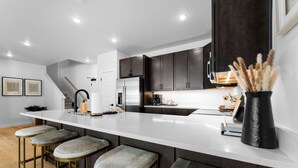 Una cocina moderna con encimera blanca, armarios oscuros y taburetes de bar.