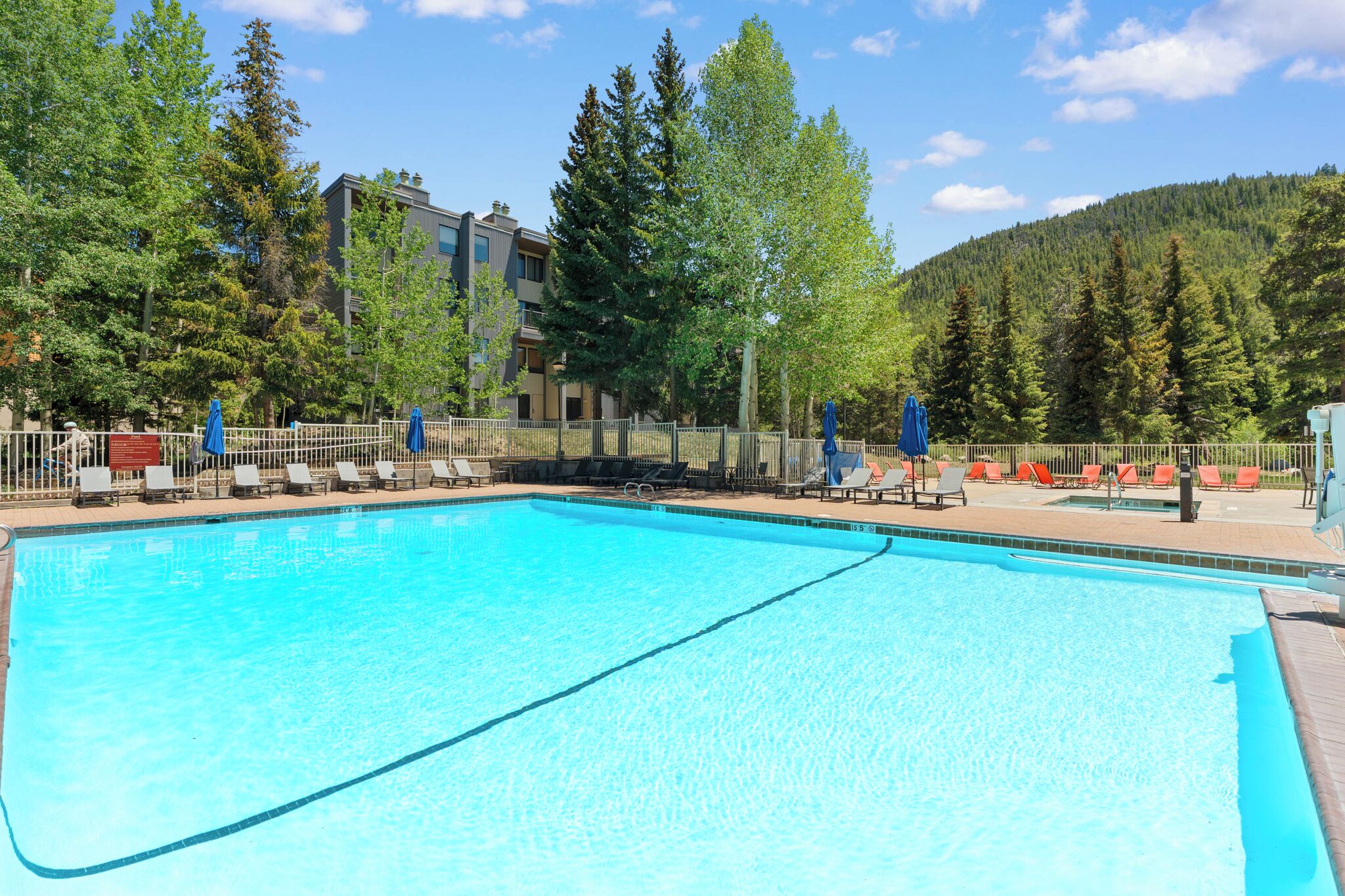Ein Swimmingpool mit Liegestühlen und einem Zaun, umgeben von Bäumen und einem Gebäude.
