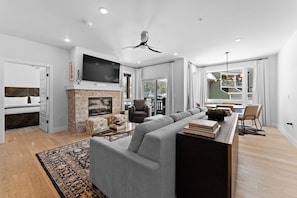 A modern living room with a fireplace, a large flat-screen TV, a ceiling fan, and a dining area with a view of the outside. - Bw2301-3 (Keystone)