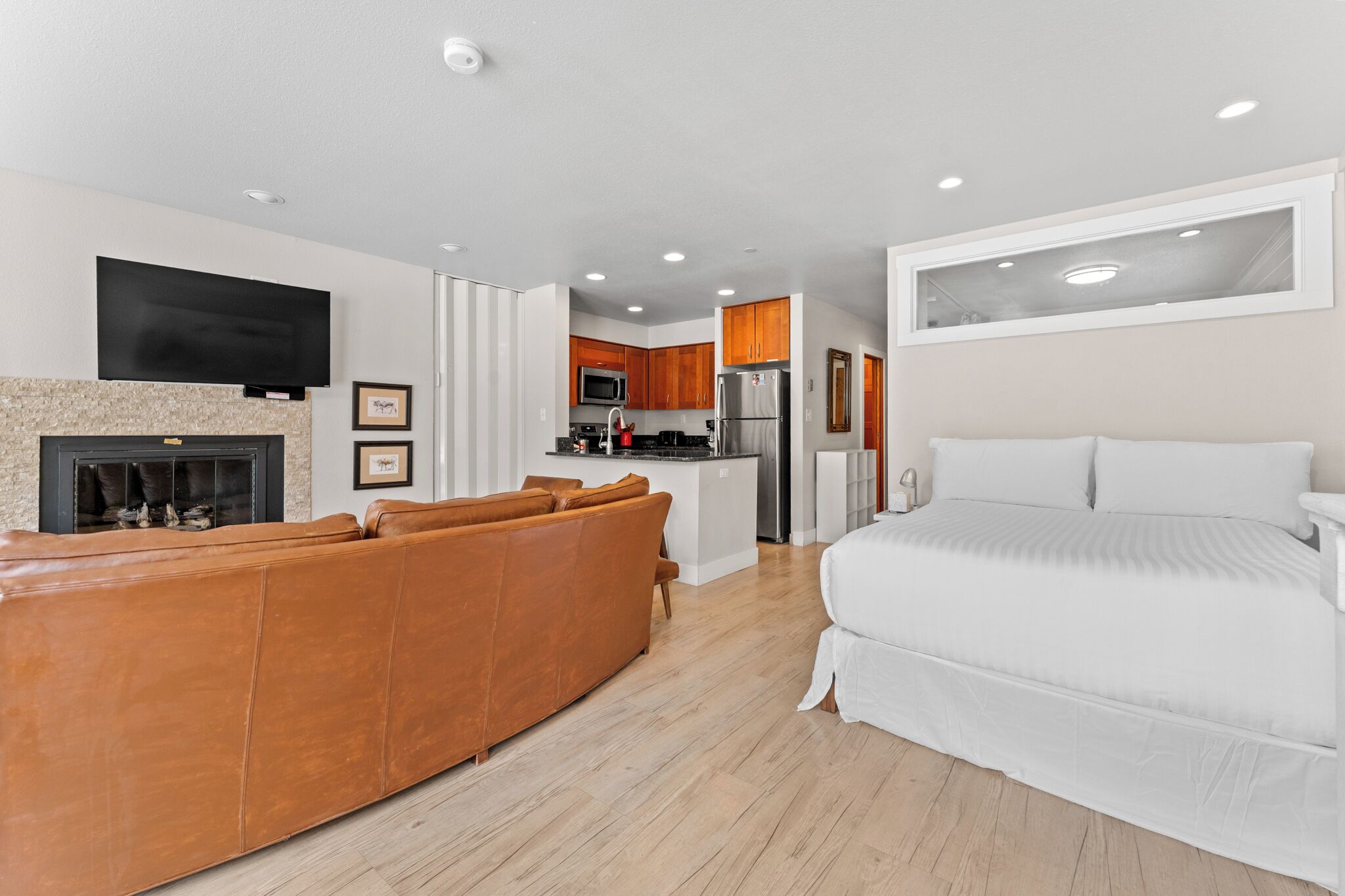 A modern hotel room with a sofa, a bed, a kitchen area, and a flat-screen TV.