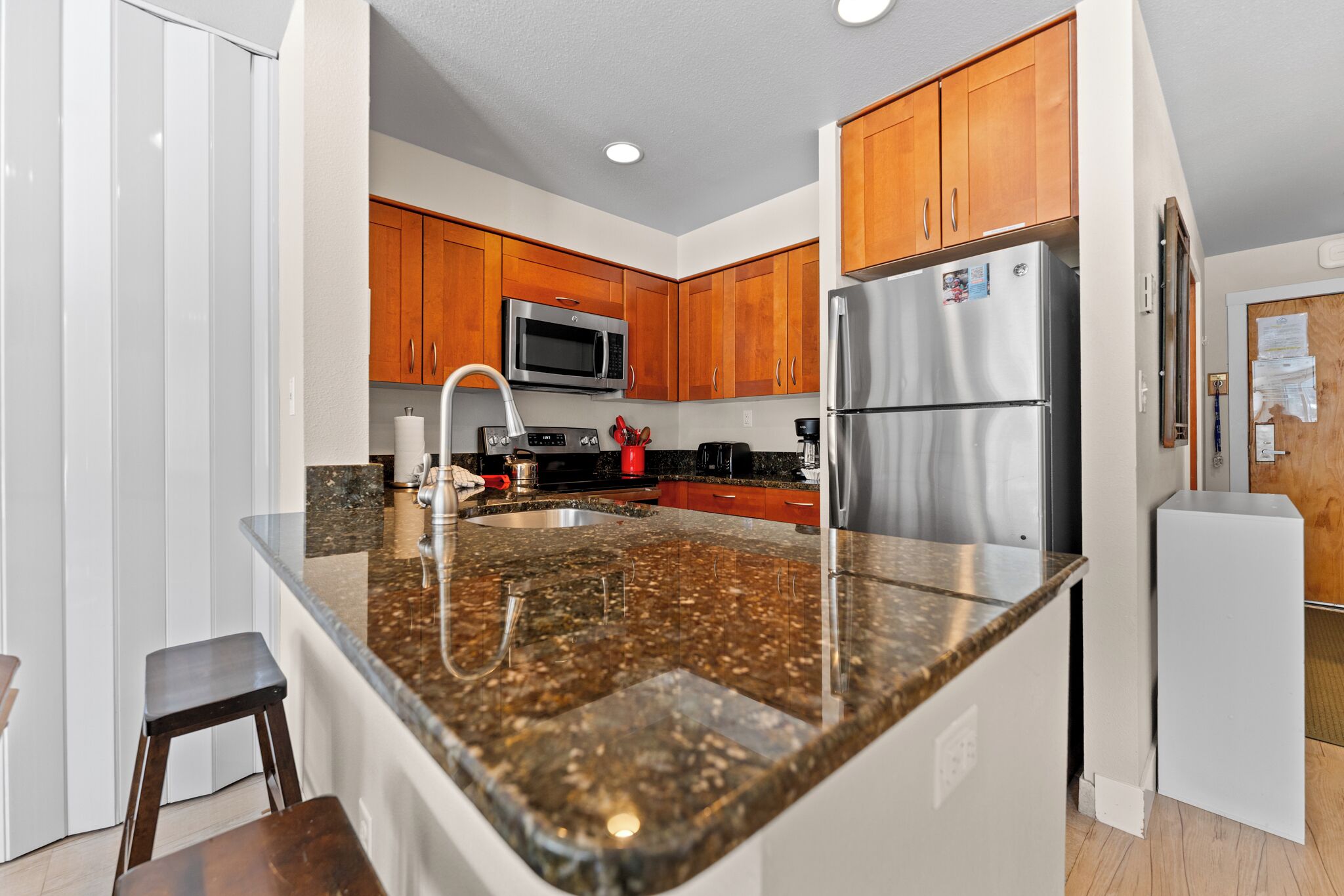 A modern kitchen with granite countertops, stainless steel appliances, wooden cabinets, and a built-in microwave.