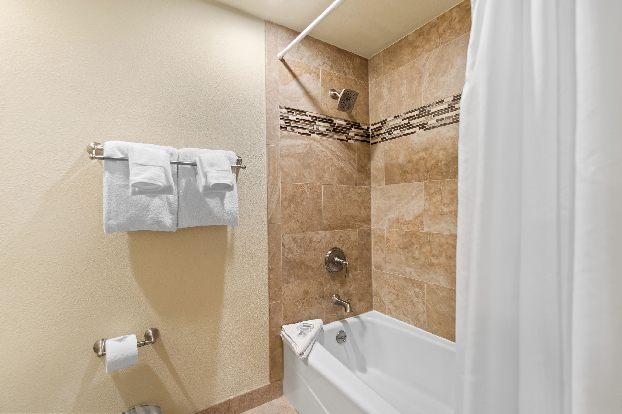 A bathroom with a bathtub, a shower, beige walls, and a towel rack with two towels.