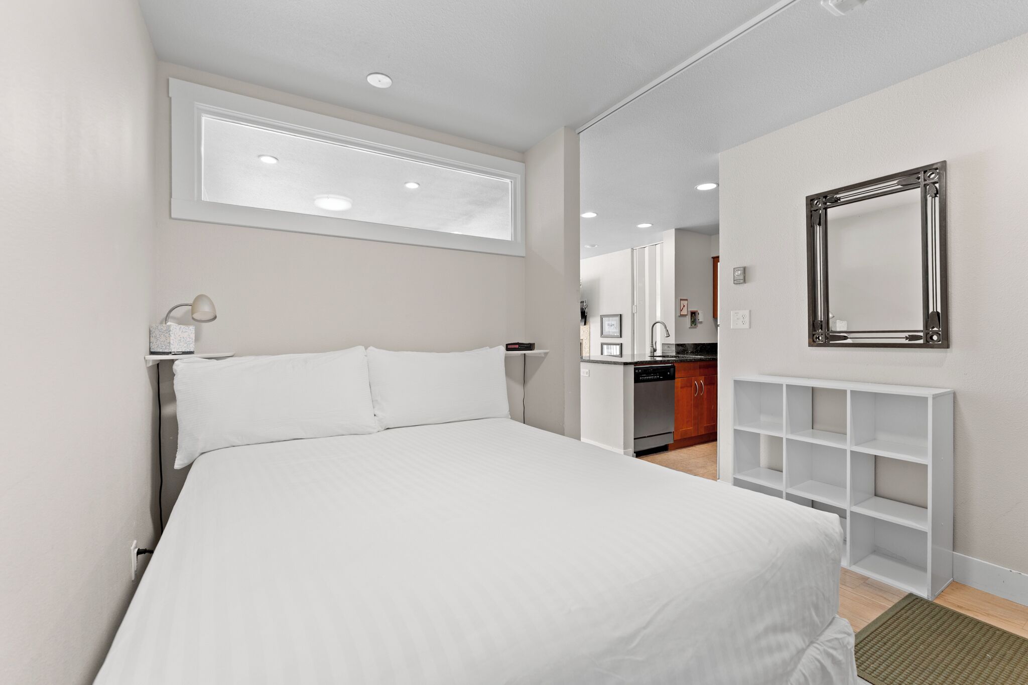 A hotel room with a bed, a desk, a mirror, and a kitchenette.