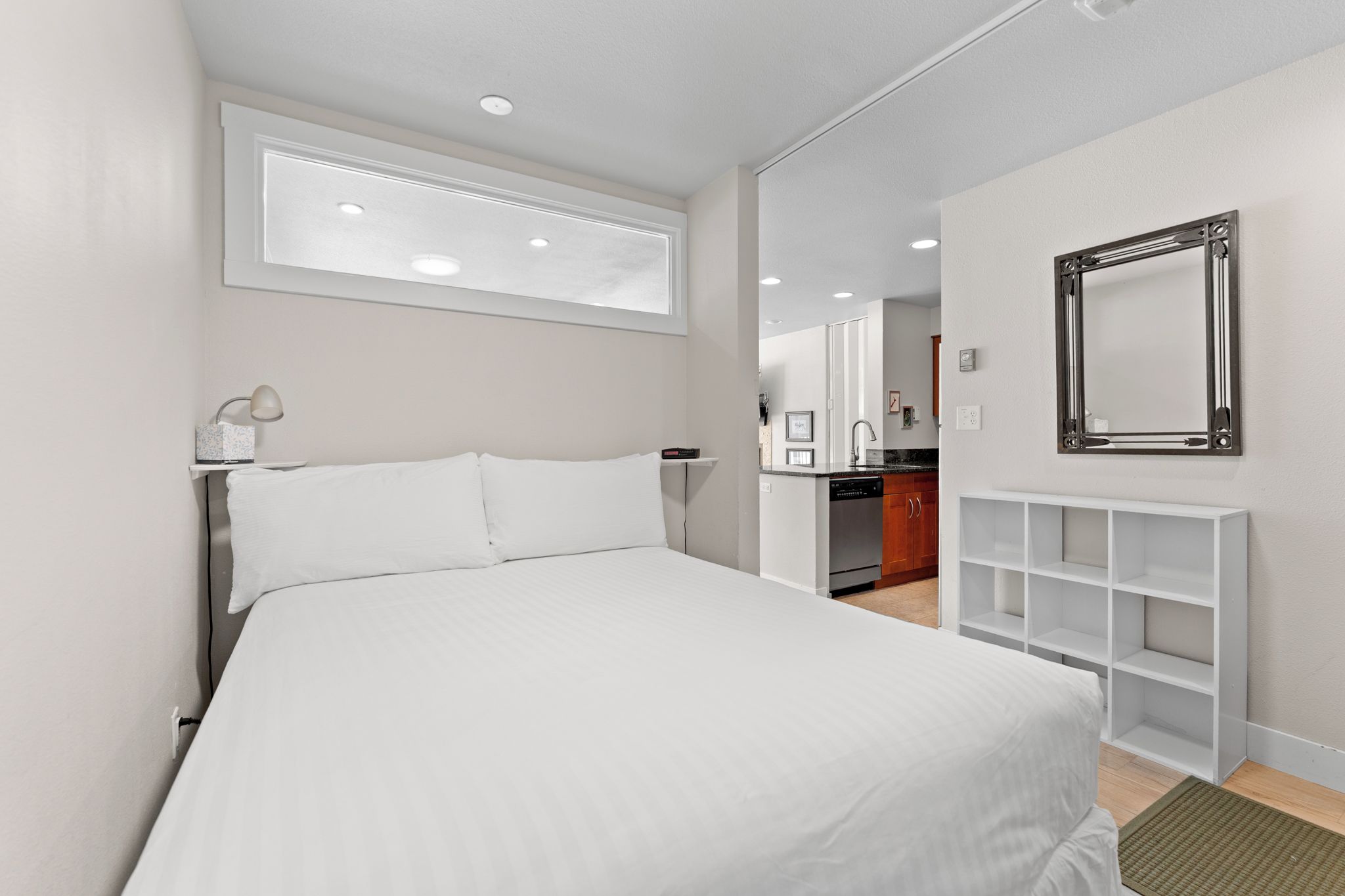 A hotel room with a bed, a desk, a mirror, and a kitchenette.