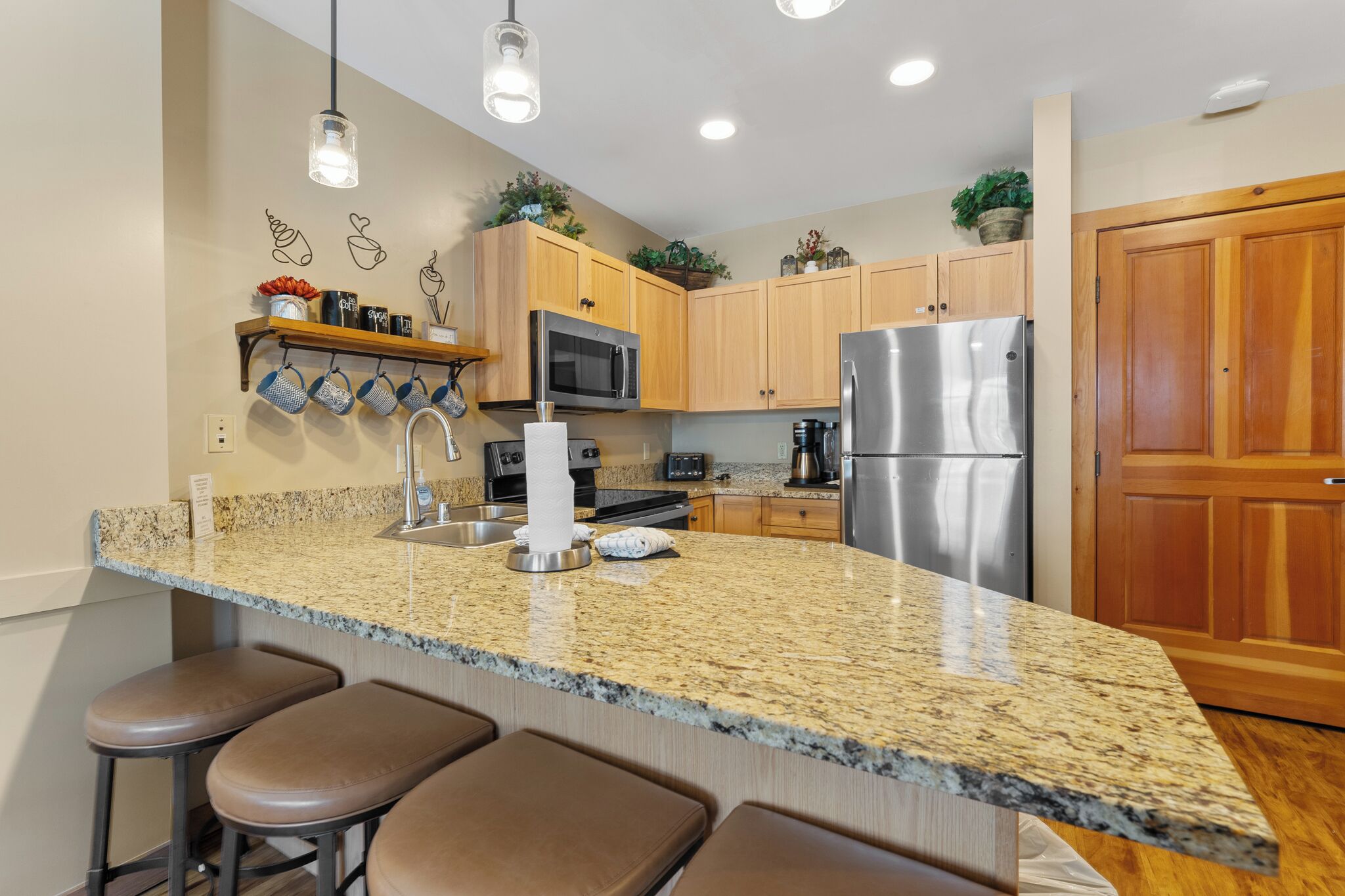 A kitchen with granite countertops, stainless steel appliances, wooden cabinets, and bar stools.