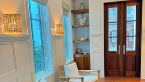 Ein Zimmer mit Holzboden, zwei Korbstühle mit Kissen, einem kleinen runden Tisch und einem dekorativen Regal mit einer Vase.