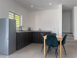 A modern kitchen with dark cabinets, a stainless steel refrigerator, and a dining area with a wooden table and teal chairs. - Compact villa central to the island (Willemstad)