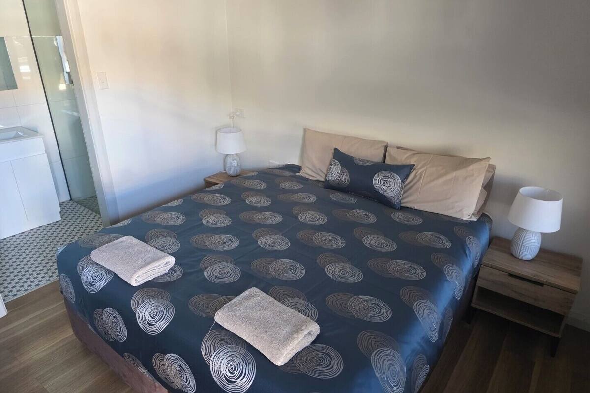 A hotel room with a large bed, two bedside tables, a nightstand, and a bathroom visible in the background.