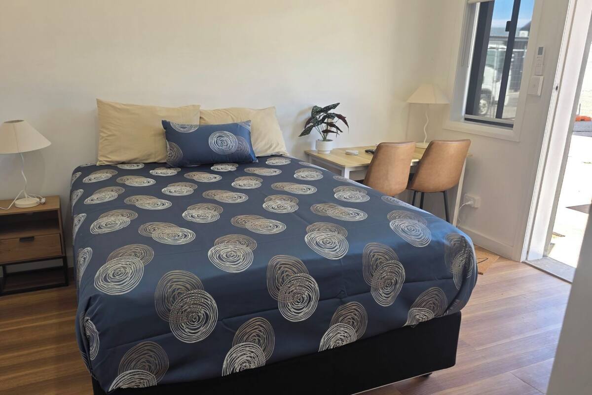 A bedroom with a bed, bedside table, lamp, and a window.