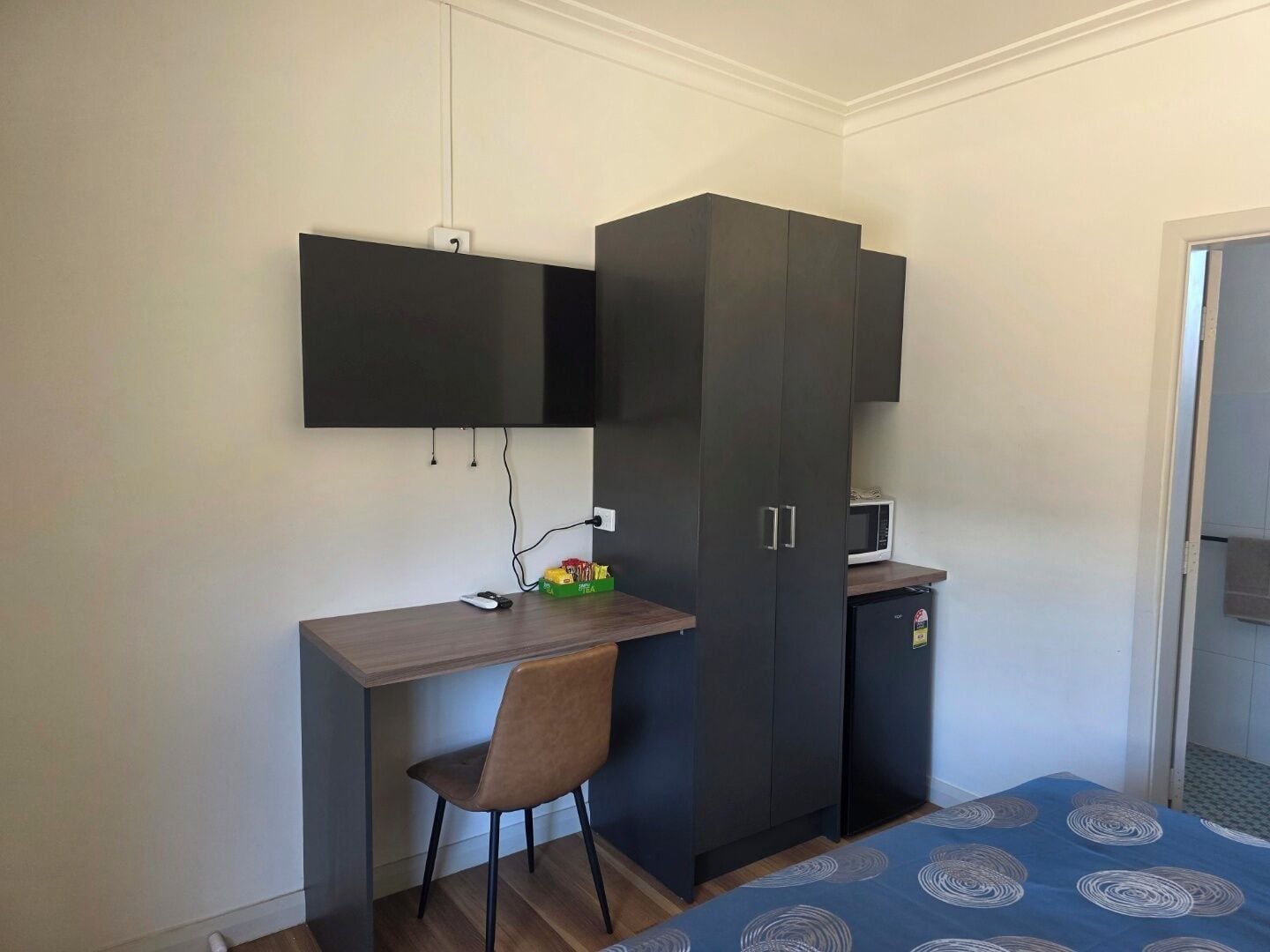 Une chambre comprenant un lit, un bureau avec une chaise, une armoire et un petit coin cuisine.