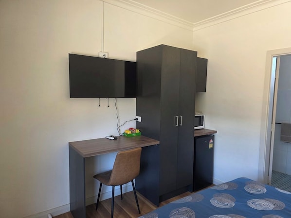 Quarto com cama, escrivaninha, cadeira, guarda-roupa e uma pequena cozinha.