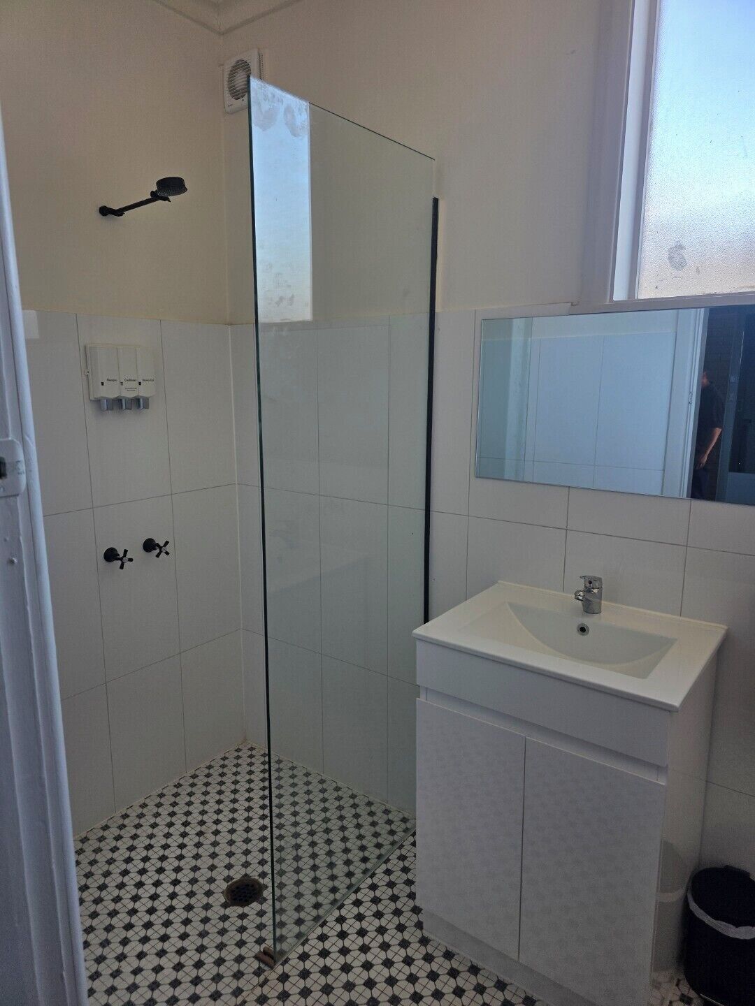 A bathroom with a glass shower enclosure, a white sink, and a tiled floor.