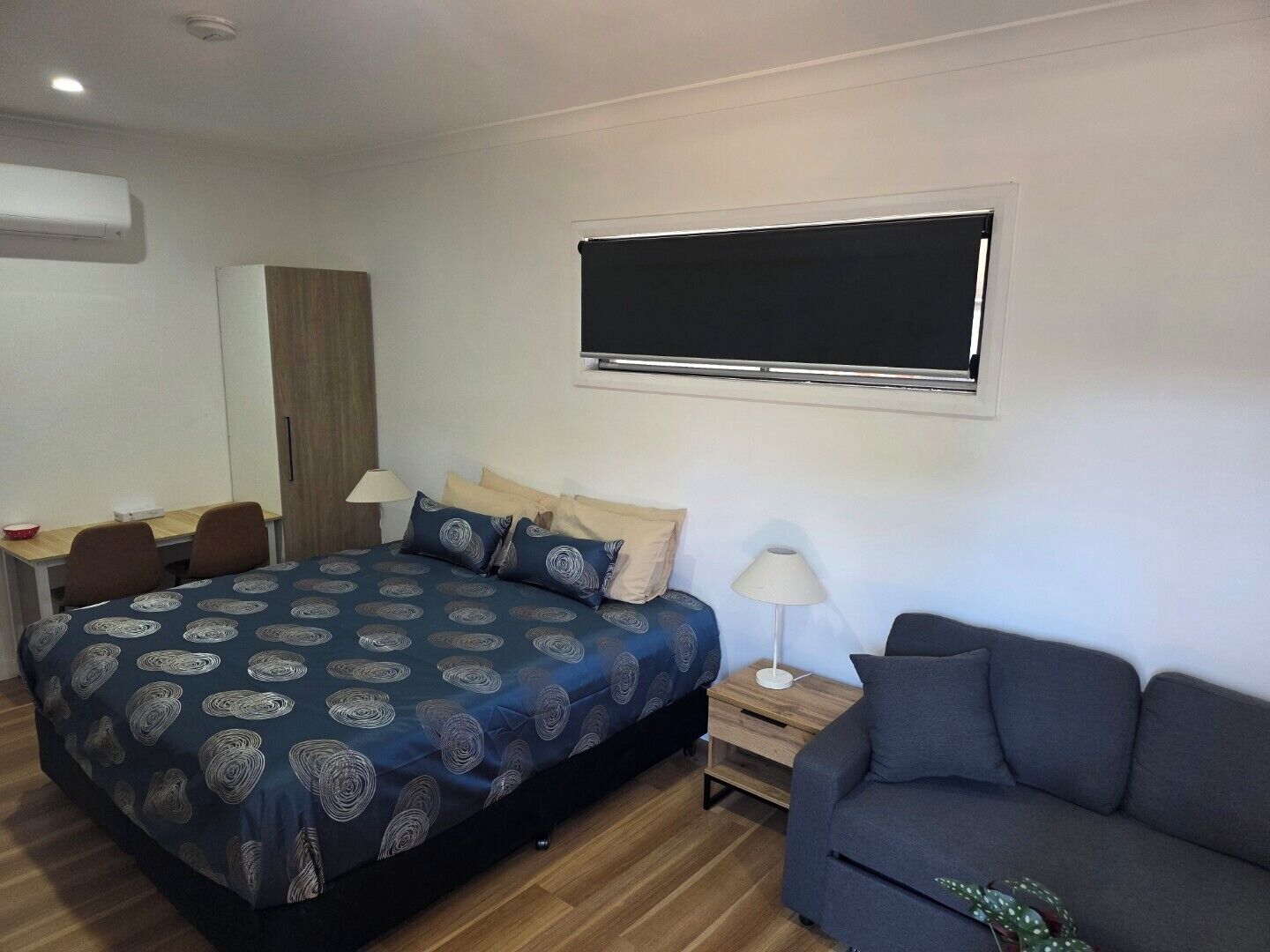 A bedroom with a bed, a desk, a chair, a sofa, and a window.