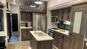Une cuisine moderne dotée d’un îlot central, d’appareils électroménagers en acier inoxydable et de meubles de rangement en bois.