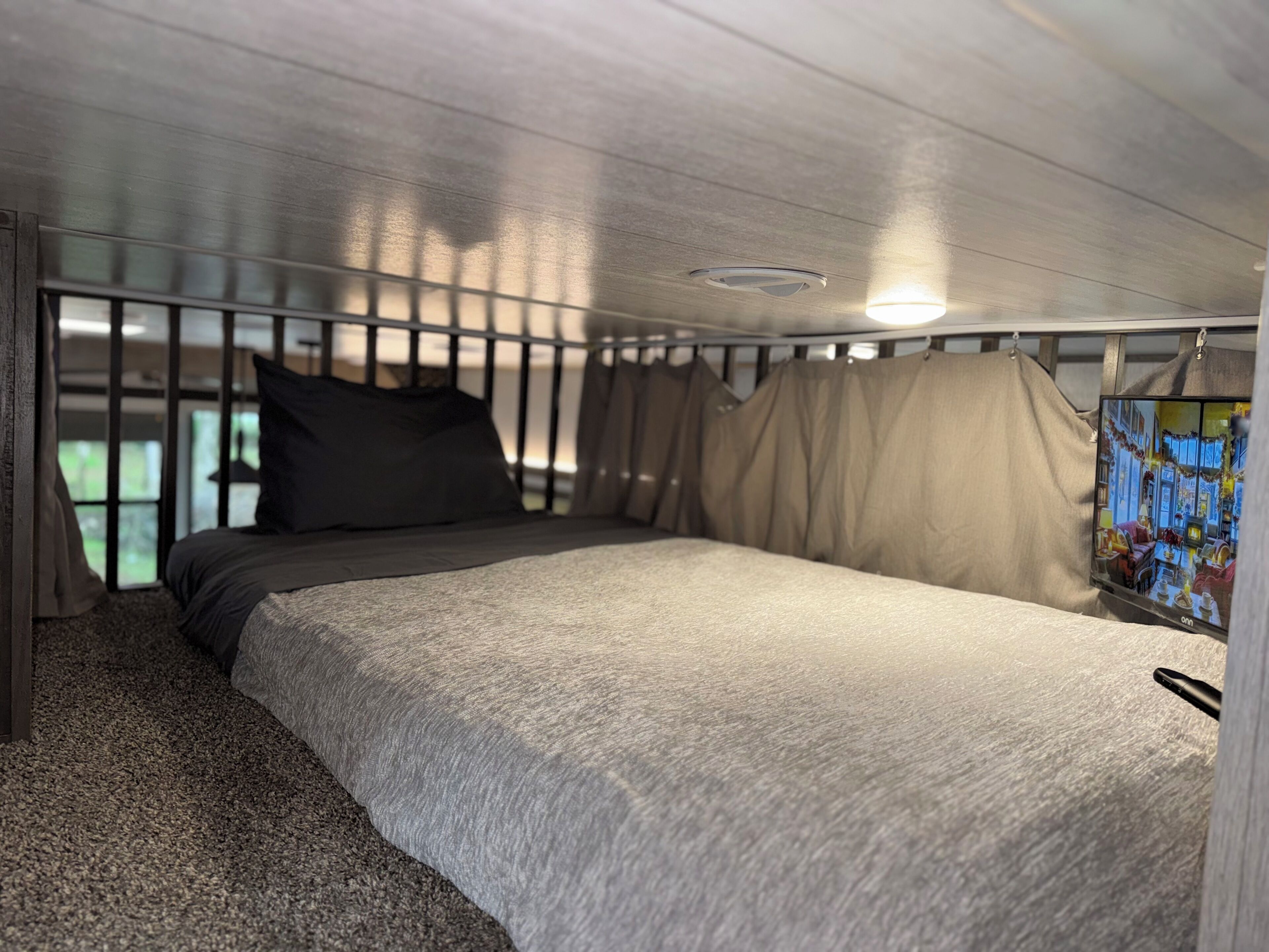 Ein Schlafzimmer mit Bett, Vorhängen, einem Fenster und einem am Wand montierten Fernseher.