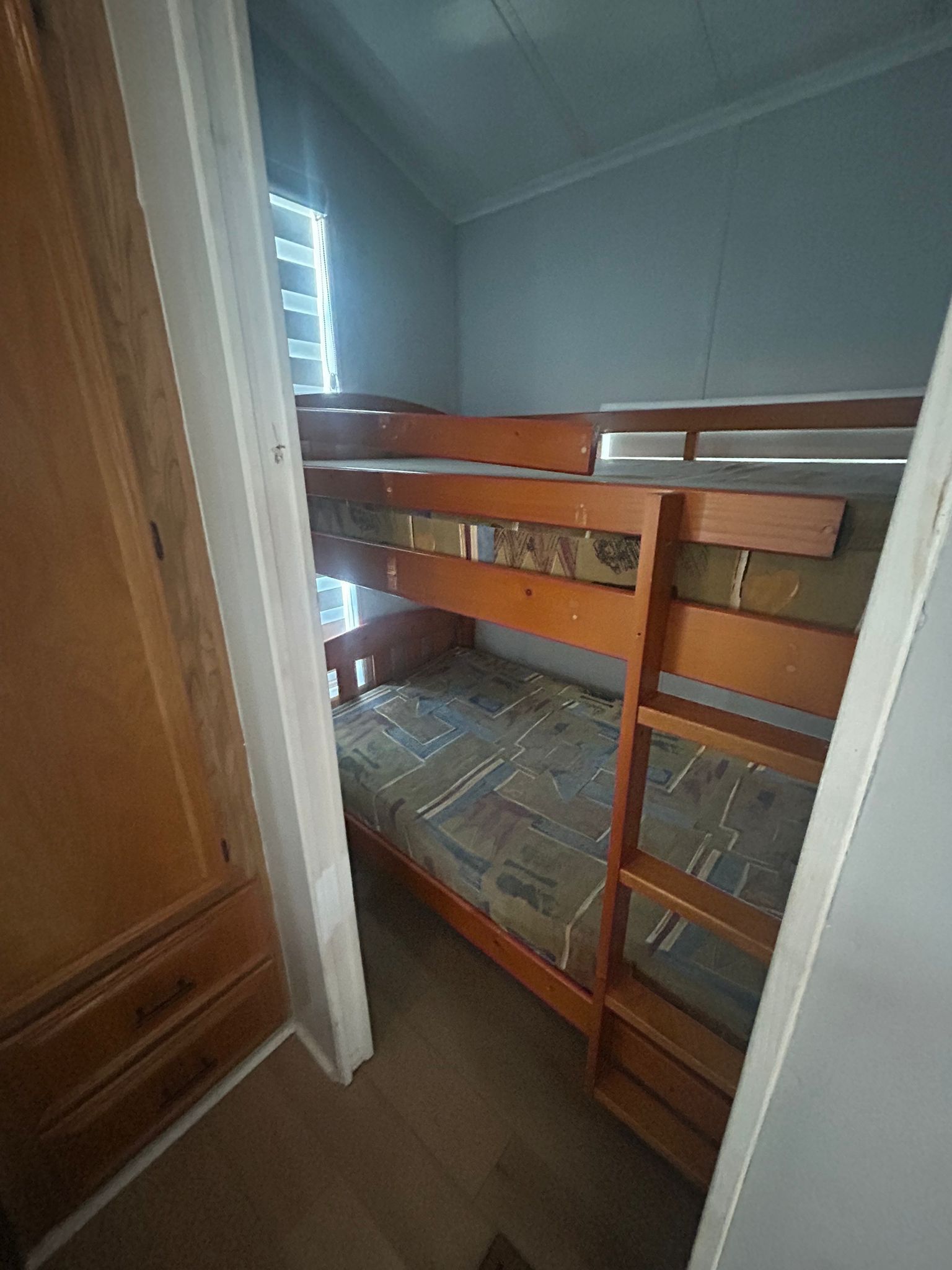 Quarto com beliche, guarda-roupa de madeira e janela.