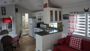 Uma cozinha compacta com armários brancos, toalha de mesa xadrez vermelha e branca, um sofá vermelho e um ventilador de teto.