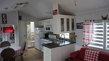 Eine kleine Küche mit weißen Schränken, einer rot-weißen karierten Tischdecke, einem roten Sofa und einem Deckenventilator.