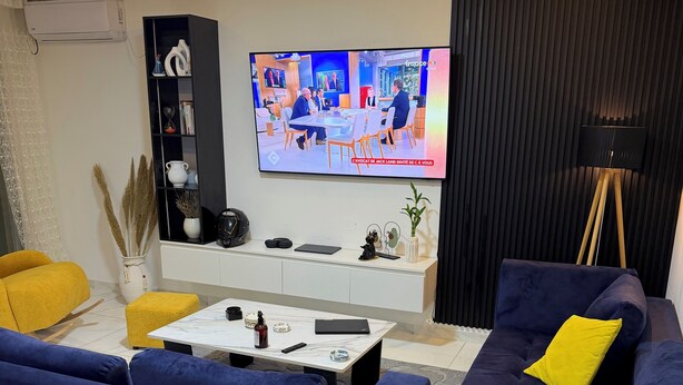 Een moderne woonkamer met een flatscreen televisie, een zithoek, een salontafel en een boekenplank.
