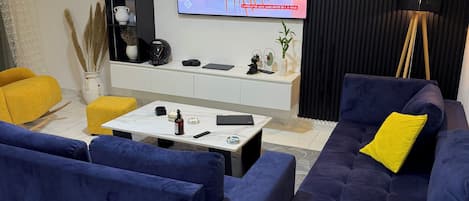 A modern living room with a flat-screen TV, a sofa set, a coffee table, and a bookshelf.