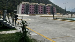 Un immeuble à plusieurs étages, doté d’un toit plat, entouré d’un parking et d’un paysage vallonné.